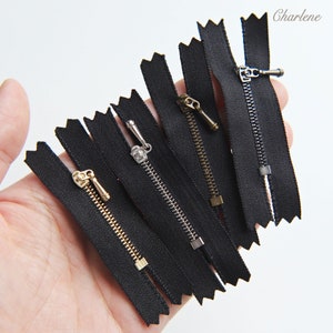 May include: A set of six black zipper pulls with different colored metal sliders. The zippers are all the same length and have a zig-zag pattern on the edges.