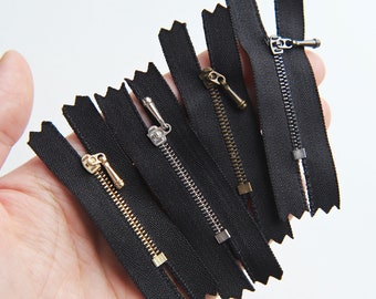 May include: A set of six black zipper pulls with different colored metal sliders. The zippers are all the same length and have a zig-zag pattern on the edges.