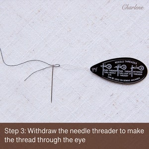 May include: A black needle threader with instructions on how to use it. The threader is being used to thread a needle with black thread.