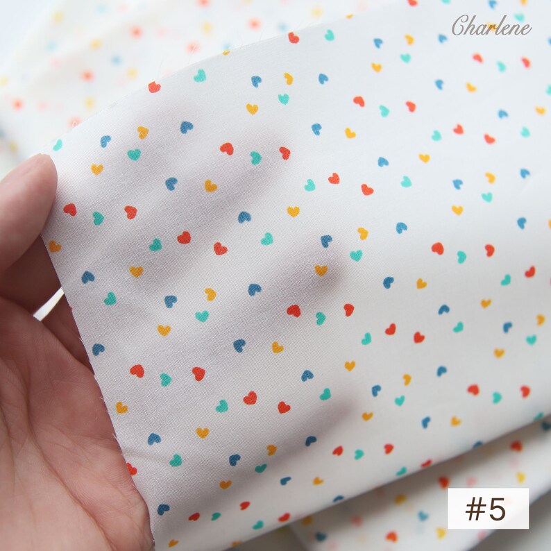 May include: White fabric with a scattered pattern of small red, blue, yellow, and green hearts. #5