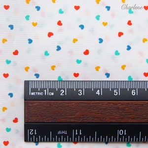 May include: White fabric with a repeating pattern of colourful hearts. The fabric is measured with a ruler in centimetres.