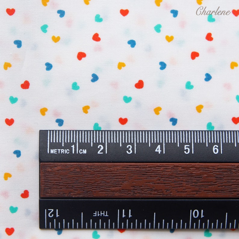 May include: White fabric with a repeating pattern of colourful hearts. The fabric is measured with a ruler in centimetres.