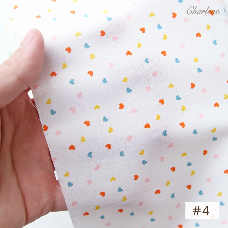 May include: White fabric with a scattered pattern of small, colourful hearts. The hearts are in shades of pink, blue, yellow, and orange. The fabric is labelled with the number "#4".