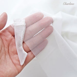 Puede incluir: Tela de malla blanca con un patrón de diamante. La tela se sostiene en una mano y es muy transparente.