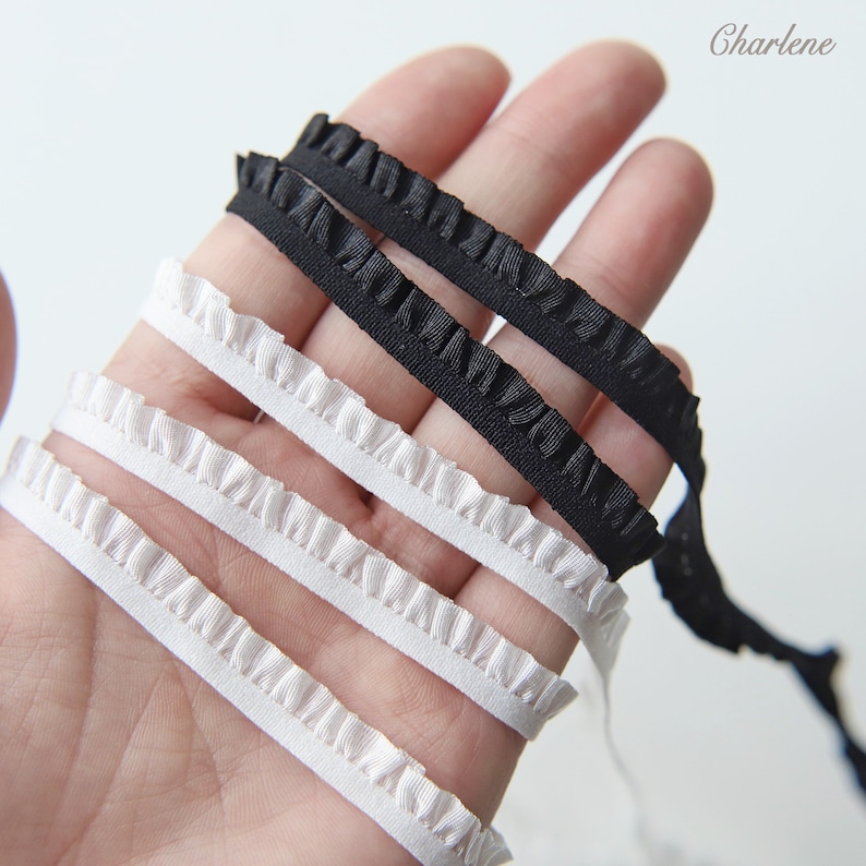 May include: Four strips of white and black ruffled trim. The trim is shown on a hand.
