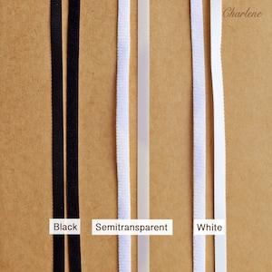 Pu&ograve; includere: Tre strisce di tessuto elastico in nero, bianco semitrasparente e bianco. Il tessuto &egrave; mostrato su uno sfondo marrone.