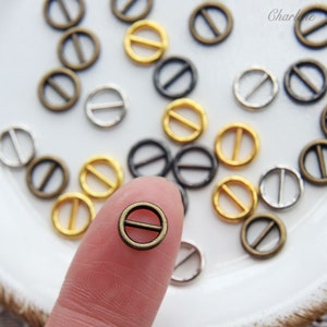 Könnte beinhalten: Sortiment kleiner Metallringe mit einem Mittelbalken. Die Ringe sind in Silber, Gold und Bronzefarben. Die Ringe haben einen Durchmesser von etwa 1,2 cm.