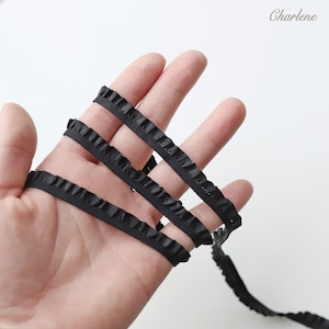 May include: Black ruffled trim ribbon. The ribbon is folded in thirds and held in a hand.