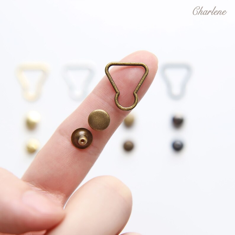 以下が含まれることがあります： ストラップやその他のアクセサリーを取り付けるための金色の金属製金具のセット。セットにはDリング、スタッド、ポストが含まれています。