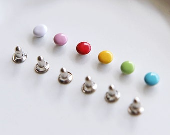 Può includere: Assortimento di bottoni rotondi colorati con basi in metallo argentato. I bottoni sono in un ordine di colori arcobaleno, a partire dal bianco, dal rosa, dal rosso, dal giallo, dal verde e dal blu.