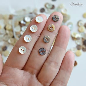 May include: Eight small round buttons with two holes each, arranged in two vertical rows. The left column features four smooth white buttons, while the right column displays four buttons with varied brown, grey, and tan marbled patterns.