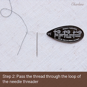 May include: A black needle threader with instructions on how to use it. The threader is on a white surface with a black thread and needle.