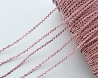 May include: A spool of dusty rose pink scalloped trim. The trim is a wavy, zig-zag pattern.