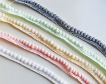 Könnte beinhalten: Fünf Spulen mit Pompon-Besatz. Der Besatz ist in verschiedenen Farben, darunter weiß, rosa, gelb, hellgrün und grau.