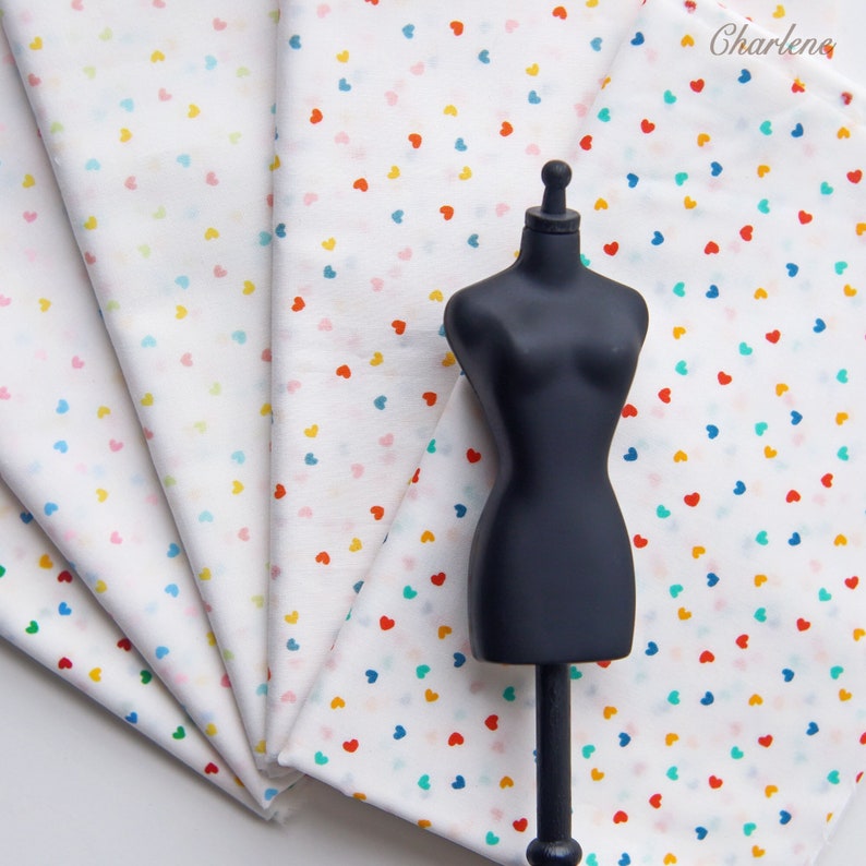 May include: A stack of white fabric with a small, colourful heart pattern. The fabric is folded in a fan shape and a black mannequin is standing in front of it.