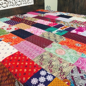 May include: A patchwork quilt featuring a vibrant array of colors and patterns. The quilt is composed of numerous rectangular fabric pieces in shades of red, pink, green, and blue, with floral and geometric designs. The quilt is a decorative bedding item.