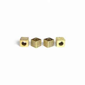 Könnte beinhalten: Vier goldfarbene, würfelförmige Perlen mit Gittermuster. Jede Perle hat ein Loch auf einer Seite. Die Perlen sind auf weißem Hintergrund in einer Reihe angeordnet. Diese Perlen könnten für die Schmuckherstellung verwendet werden.