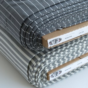 May include: Two rolls of gray and white striped knit fabric. The fabric is folded and stacked on top of each other. The fabric is labeled "Striped Knits" and "AGF" on the packaging.