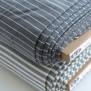 May include: Two rolls of striped fabric, one gray and white, and one white and gray. The fabric is rolled up and the ends are visible.