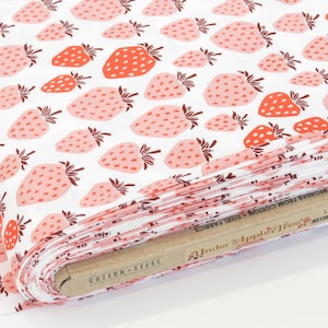 May include: A roll of white cotton fabric printed with a repeating pattern of strawberries. The strawberries are in shades of pink and red with green stems. The fabric is labeled "Cotton + Steel Fabrics".