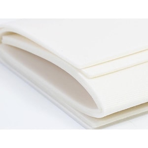 May include: Close-up of a stack of white, rectangular, folded fabric sheets. The sheets are layered, with a slight curve visible on the edges. The fabric appears to be soft and smooth, with a subtle texture. The background is plain white.