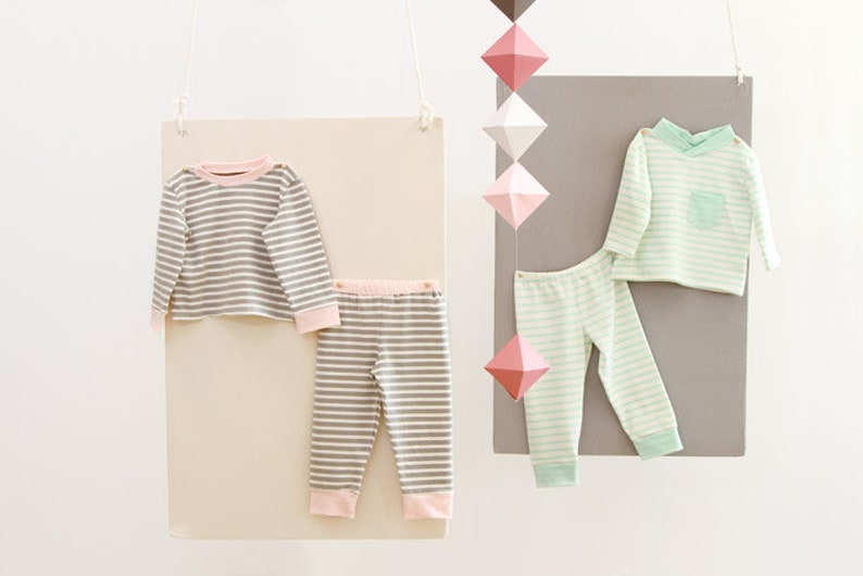 May include: Two sets of striped pajamas for children. One set is gray and white with pink trim, the other is light green and white with green trim.