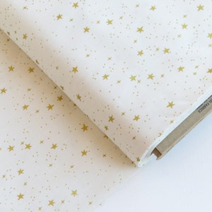 May include: Off-white fabric with a repeating pattern of gold stars and small dots. The fabric is folded, revealing a glimpse of the cardboard packaging. The fabric is made from cotton and steel fabrics.