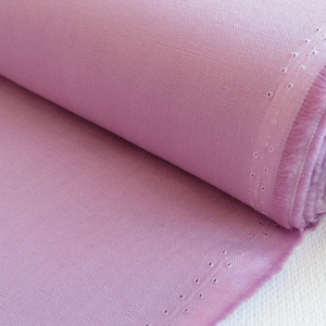 May include: A roll of light purple fabric. The fabric has a woven texture and a raw edge with small, evenly spaced holes. The fabric is tightly rolled, revealing the texture and color.