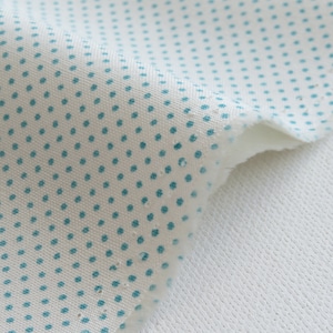 May include: Close-up of a piece of white fabric with a pattern of small, evenly spaced teal dots. The fabric is layered over a white, textured material, creating a contrast in textures. The edges of the fabric are frayed.