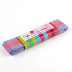 May include: Rolled lavender webbing with a colorful striped label that reads "Tula Pink Webbing by renaissance ribbons." The webbing has stripes of coral, pink, blue, and green. The product is likely used for crafting or sewing projects.