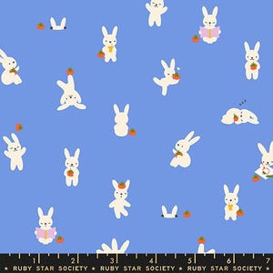 May include: A blue fabric featuring a repeating pattern of white rabbits in various poses, some holding small orange tomatoes. A black ruler at the bottom shows measurements from 1 to 7 inches, with the text Ruby Star Society printed repeatedly.
