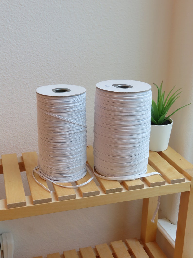 Puede incluir: Dos carretes de cord&oacute;n el&aacute;stico blanco en un estante de madera. Los carretes est&aacute;n envueltos en papel blanco y tienen un cord&oacute;n el&aacute;stico blanco enrollado alrededor de ellos.