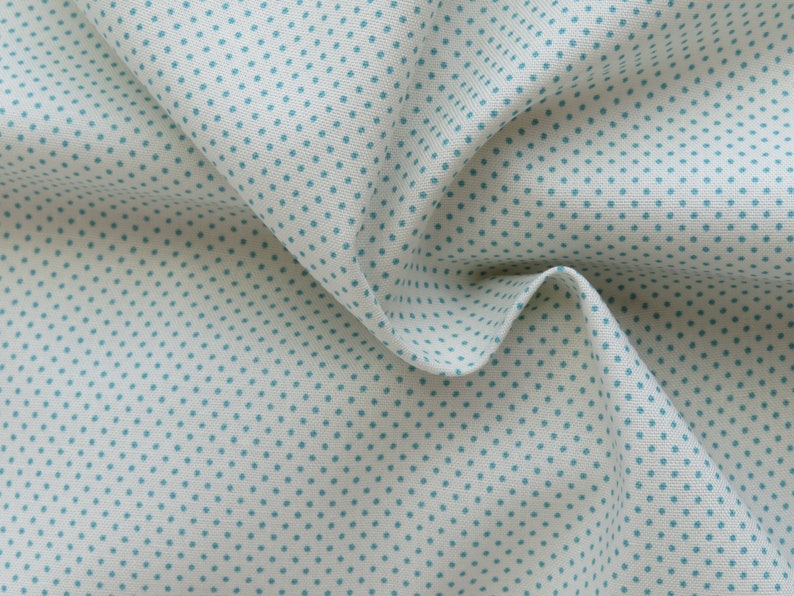 May include: Close-up of a white fabric with a repeating pattern of small, teal-colored polka dots. The fabric is folded, creating shadows and highlighting the texture of the material. The overall appearance is soft and inviting, suitable for various craft projects.