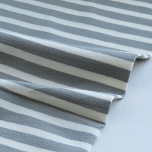 May include: Gray and white striped fabric with a soft, textured feel. The fabric is folded and draped, showing the pattern and texture.