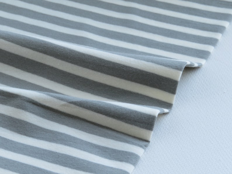 May include: Gray and white striped fabric with a soft, textured feel. The fabric is folded and draped, showing the pattern and texture.