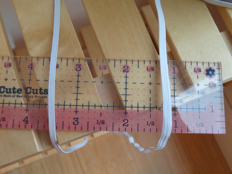 Puede incluir: Cord&oacute;n el&aacute;stico blanco medido con una regla. La regla muestra medidas en pulgadas y fracciones de pulgada. El cord&oacute;n el&aacute;stico mide aproximadamente 3 pulgadas de largo.