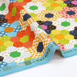 以下が含まれることがあります： オレンジ、青、緑、ピンクの六角形と花柄のパッチワークデザインのカラフルな生地。生地には、テキスト「catnap」と「stitch in time save」が入った水色の縁取りがあります。