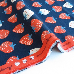 May include: Navy blue fabric featuring a strawberry design in red and white. The strawberries have green stems. A red border with text and strawberry illustrations is visible.