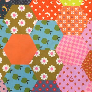 May include: A colorful patchwork fabric with a variety of hexagonal patterns. The fabric features floral, fruit, and star designs in shades of orange, blue, pink, and green. The fabric is likely used for quilting or other craft projects.