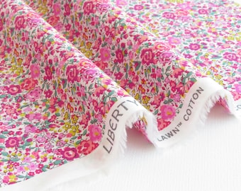 Puede incluir: Primer plano de una tela floral con fondo blanco. La tela está cubierta con un patrón de pequeñas flores rosas y magenta con hojas verdes y acentos amarillos. El borde de la tela tiene una etiqueta blanca que dice "LIBERTY LAWN COTTON".