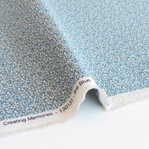 May include: A close-up of a blue fabric with a white floral pattern. The fabric has a label that reads "Creating Memories - 130131 Brie Blue".