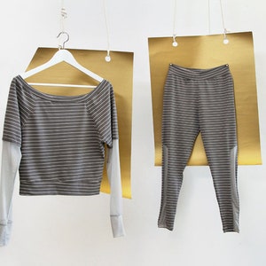 May include: A striped gray and white long-sleeved shirt and matching pants hanging on hangers against a gold background.