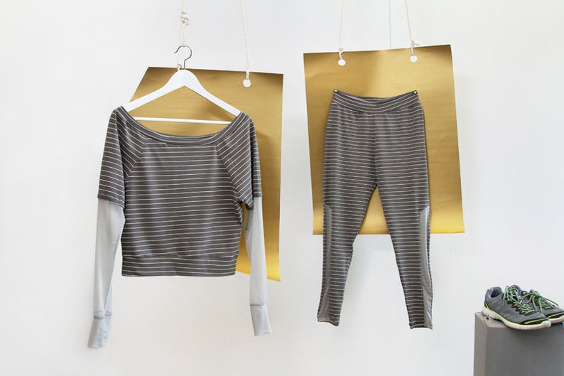 May include: A striped gray and white long-sleeved shirt and matching pants hanging on hangers against a gold background.