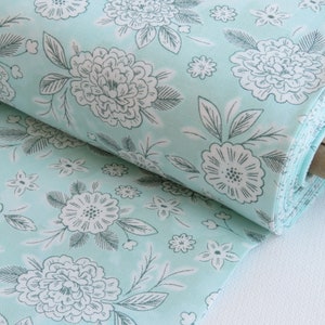 May include: A roll of light blue fabric with a white floral pattern. The fabric is folded and rolled up, with the end of the roll visible.