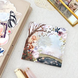 Può includere: Una stampa artistica quadrata raffigurante una fata in una scena di foresta fantastica con un fiume, fiori e un albero con lanterne appese. La stampa utilizza una morbida tavolozza di colori pastello con tonalità rosa, blu e verdi.