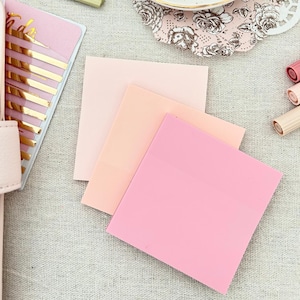 Pode incluir: Três notas adesivas rosa pastel, a maior é rosa, a do meio é pêssego e a menor é laranja claro.