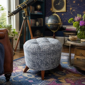 May include: A round, gray upholstered ottoman with a constellation pattern. The ottoman has a tufted top and sits on three wooden legs. The room has a telescope, globe, and books, suggesting a celestial or study theme.