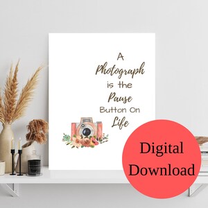 May include: A digital download of a printable quote about photography. The quote reads "A photograph is the pause button on life". The quote is accompanied by a watercolor illustration of a vintage camera with pink and brown accents and floral details.