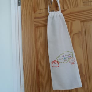 May include: White cotton drawstring bag with a green cloud embroidered with the text "Le manger est le fin de la fête". The bag is hanging on a wooden door.
