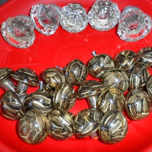 Może przedstawiać: Kolekcja 18 ozdobnych gałek drzwiowych. Gałki wykonane są z przezroczystego szkła z wzorem nasion słonecznika. Gałki ułożone są w kółko na czerwonej powierzchni.